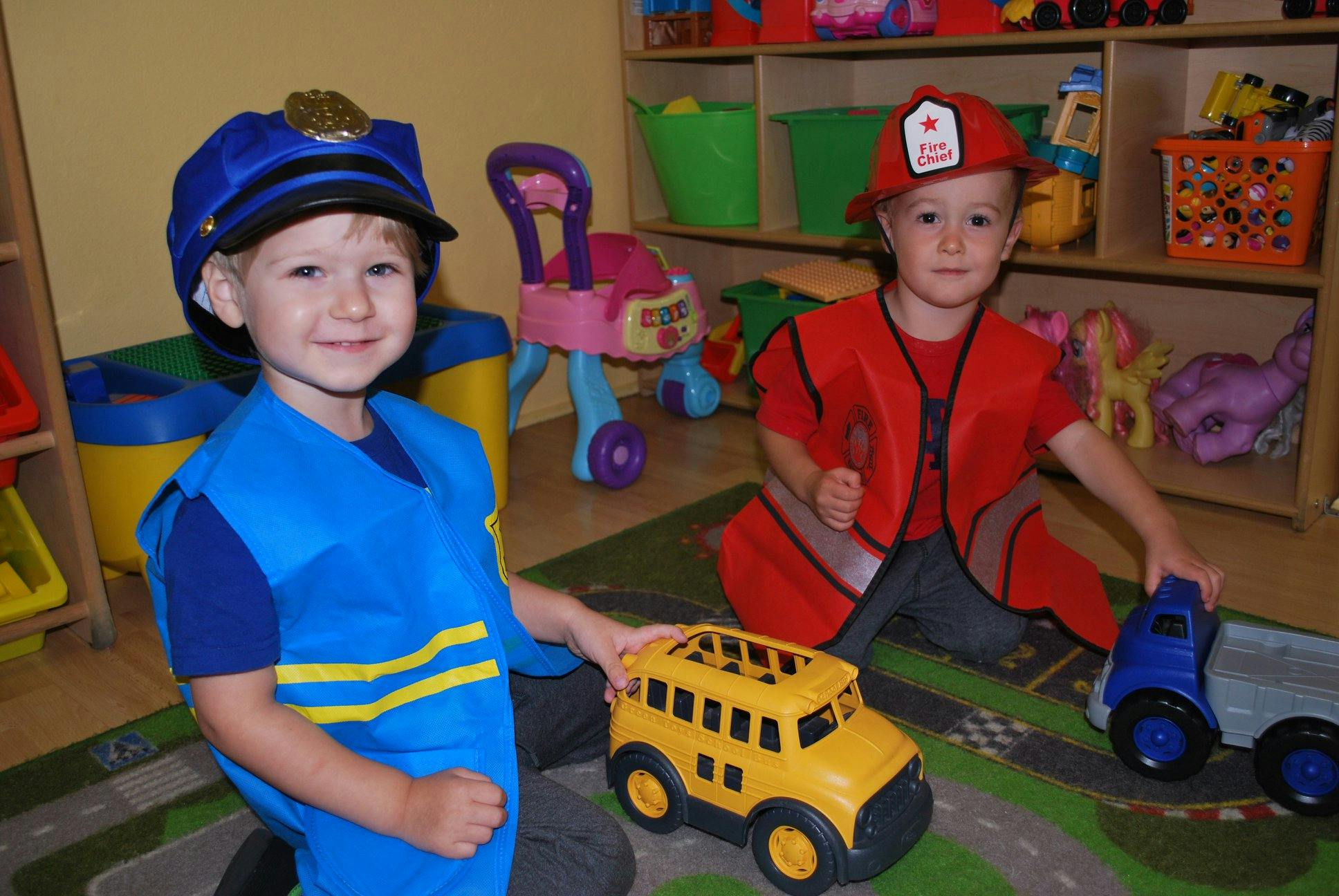 Two children in costumes playing with toy vehicles