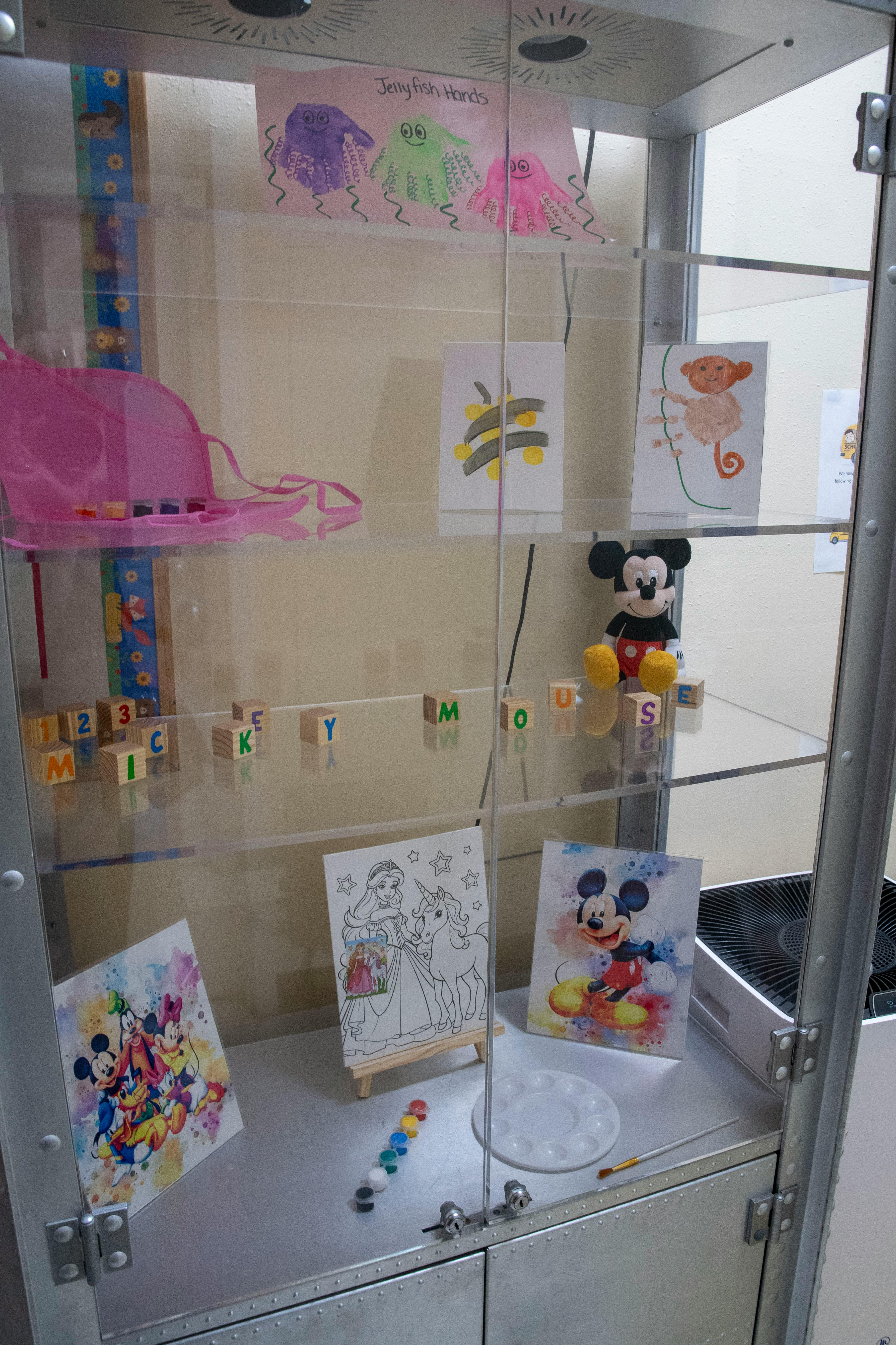 Display case with children's artwork, alphabet blocks, and a Mickey Mouse plush toy