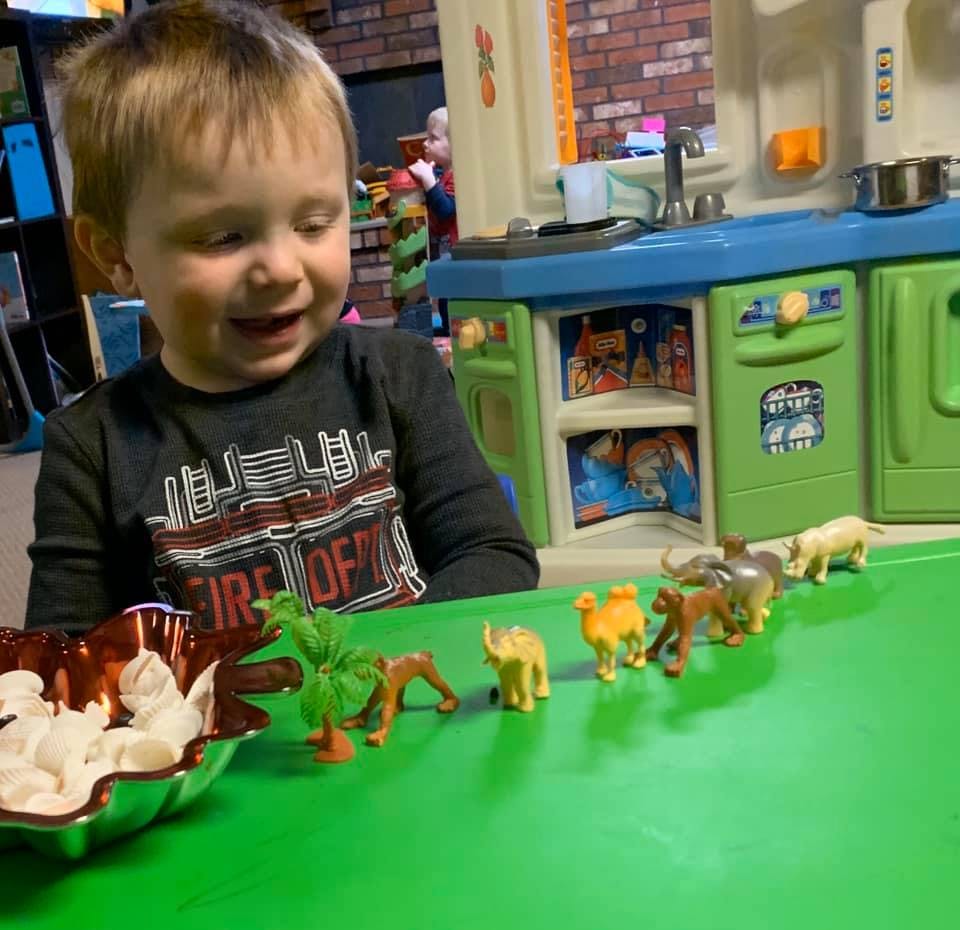 Child playing with animal figurines on a green table