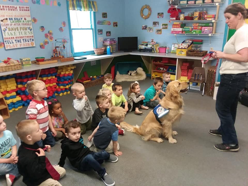 Person and children sitting on floor with a dog in a classroom