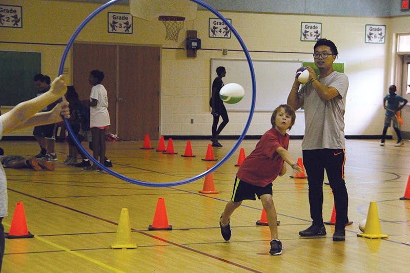 Child throwing a ball through a hoop held by another person in a gym