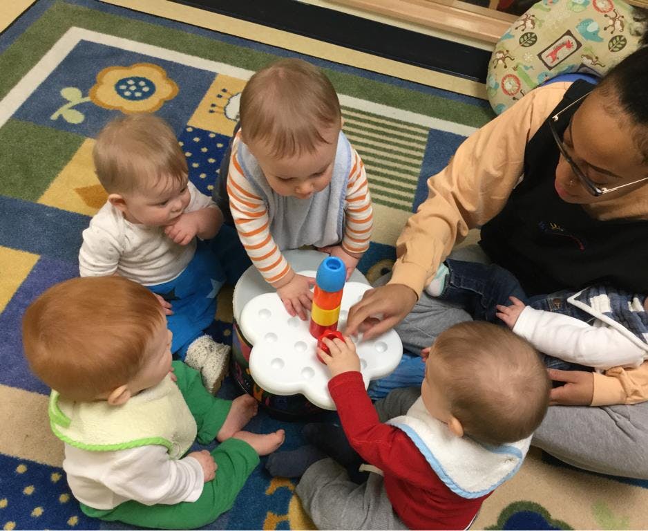 Adult and four children playing with a stacking toy on a colorful rug