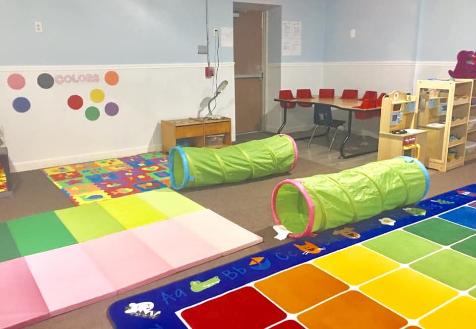 Playroom with colorful mats, play tunnels, and small tables with chairs
