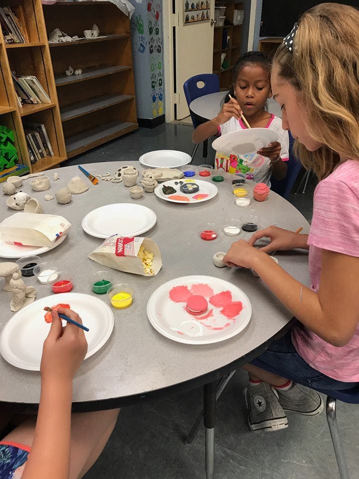 Children painting small objects at a table