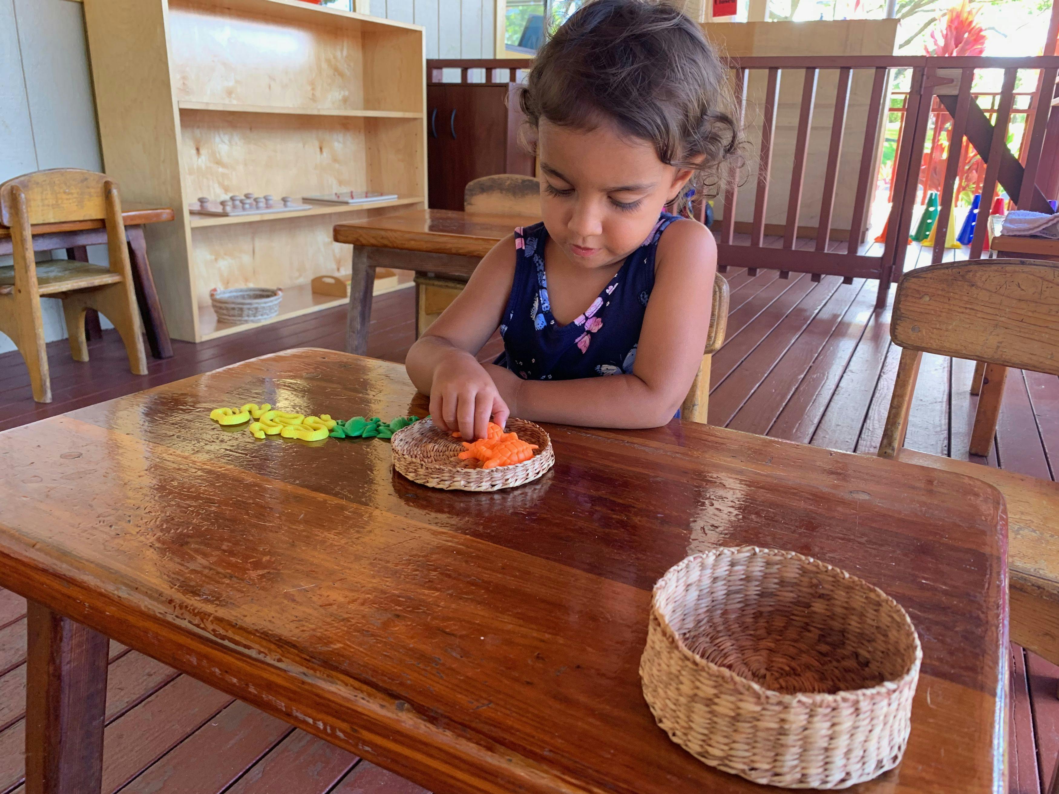 Child sorting small objects into a woven basket at a table