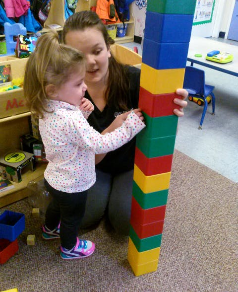 Adult and child building a tall tower with colorful blocks
