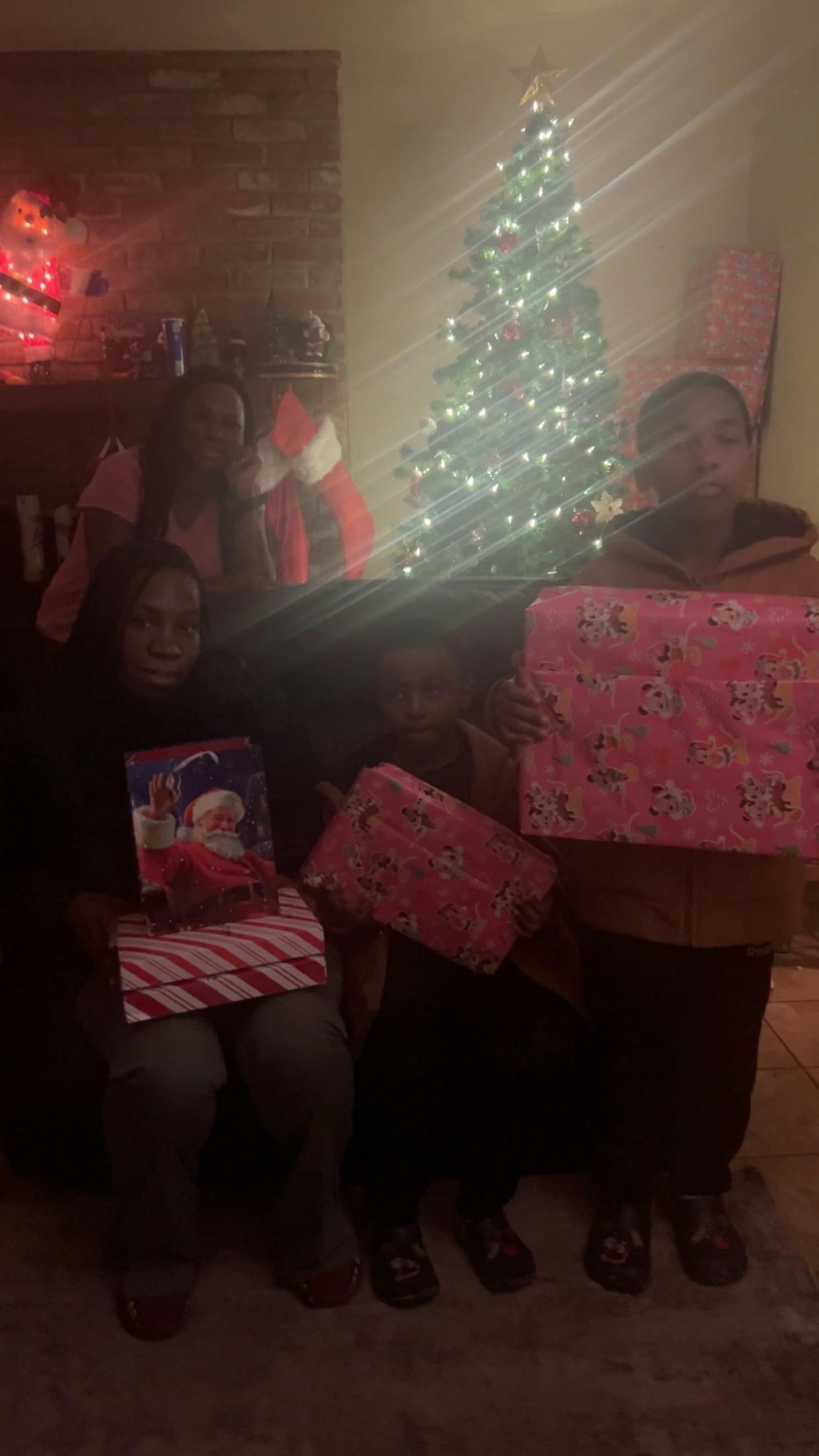 Four people holding wrapped gifts in front of a Christmas tree
