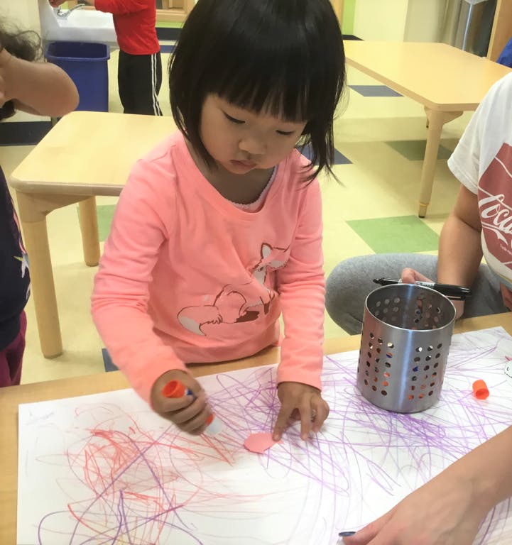 Child drawing on paper with crayons in a classroom