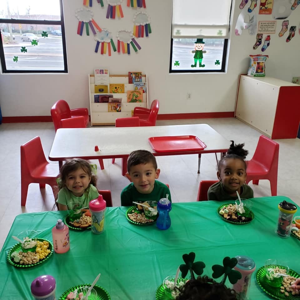 Three children sitting at a table with plates of food in a classroom