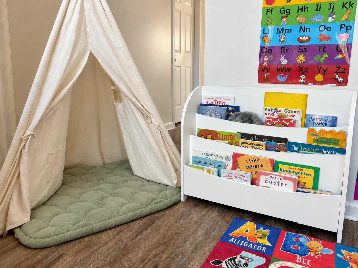 Play tent with green mat next to a children's bookcase and alphabet poster