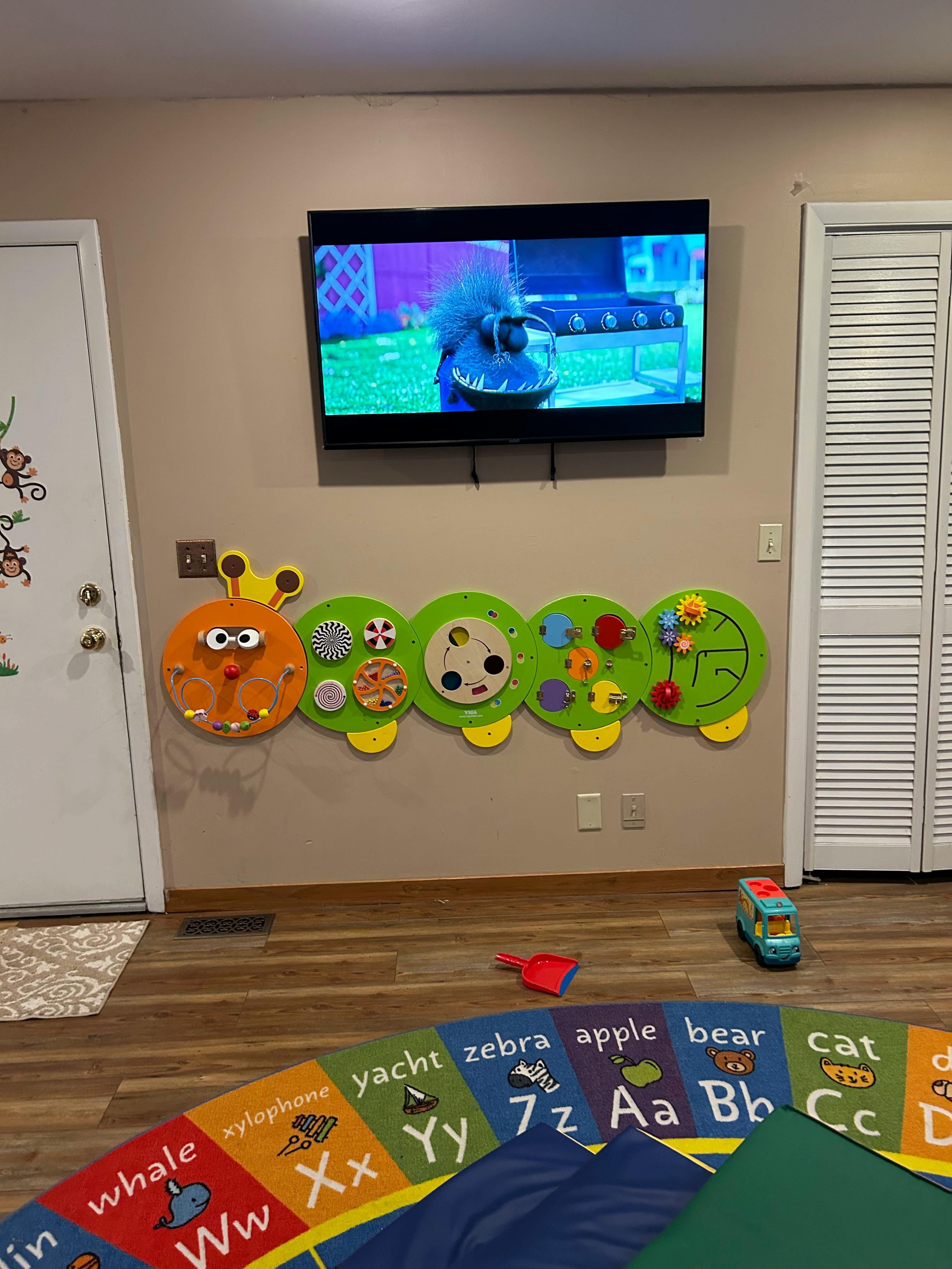 Wall-mounted caterpillar activity board above an alphabet rug