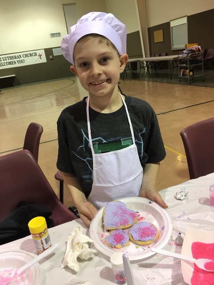 Child in chef hat and apron holding a plate of decorated cookies