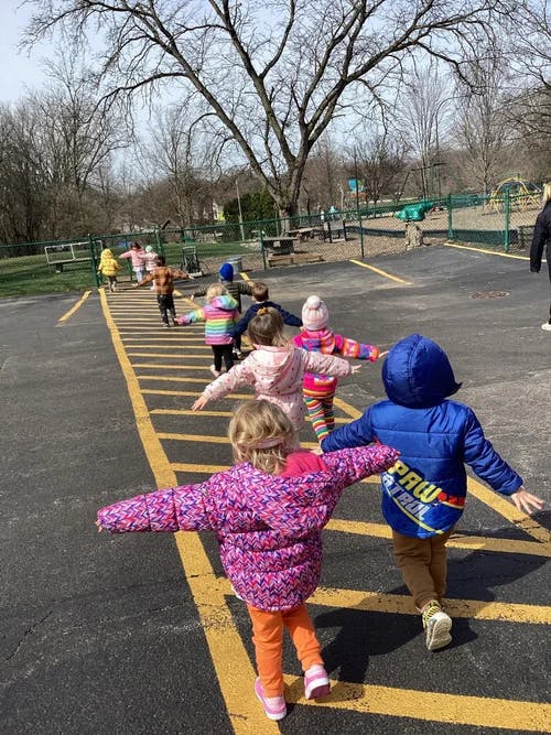 Children walking on painted yellow lines with arms outspread