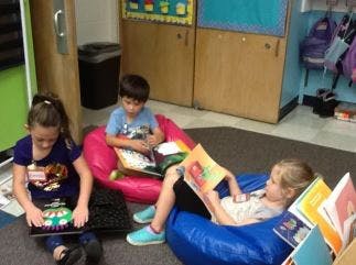 Three children reading books in a classroom