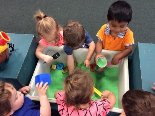 Children playing in a sensory bin with green material and toys