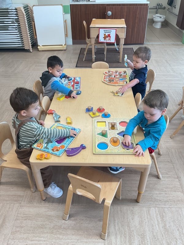 Children sitting at a table working on wooden puzzles in a classroom