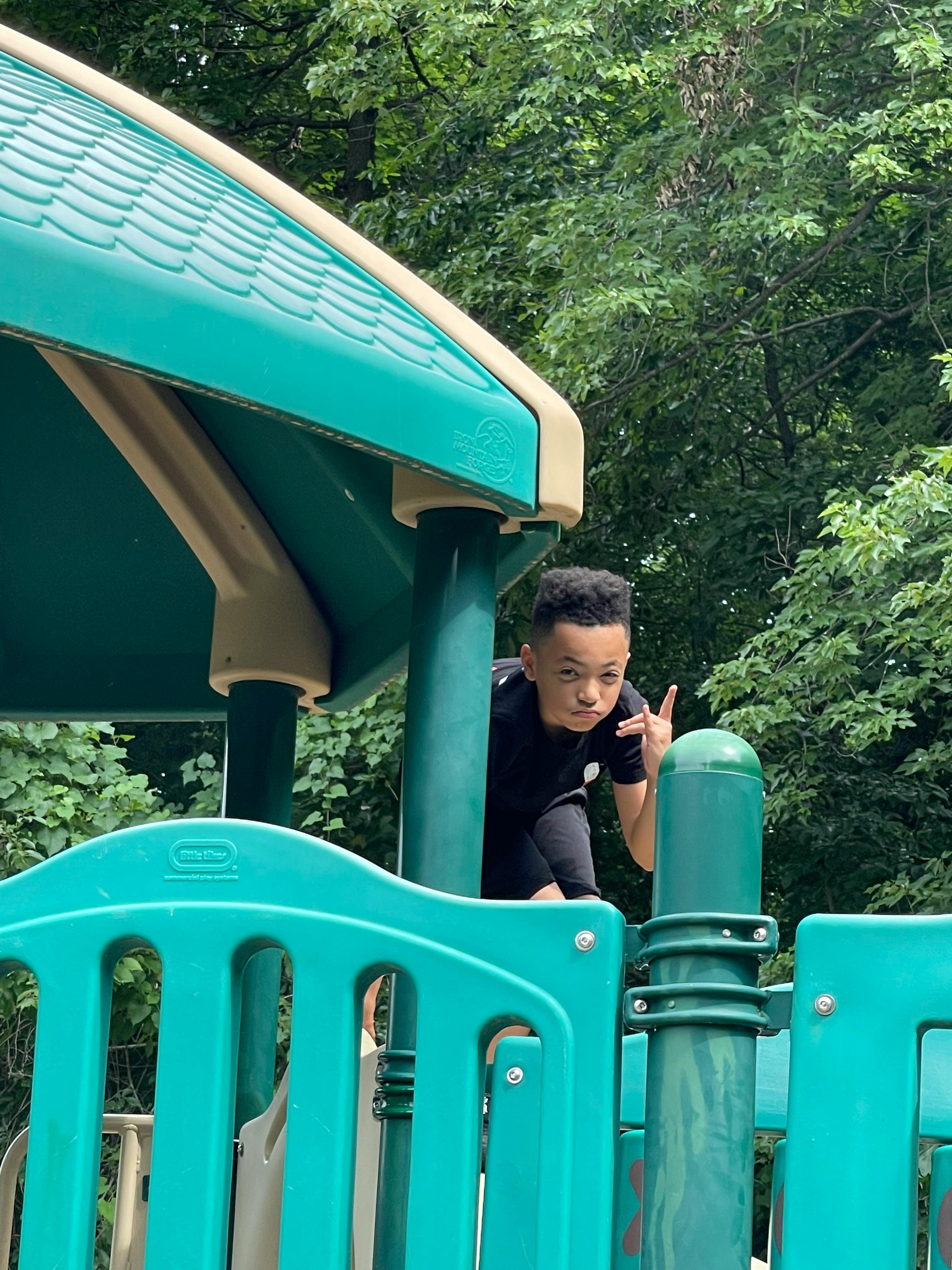 Child on a playground structure making a hand gesture