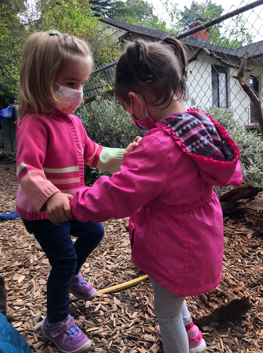 Two children wearing face masks and holding hands outdoors