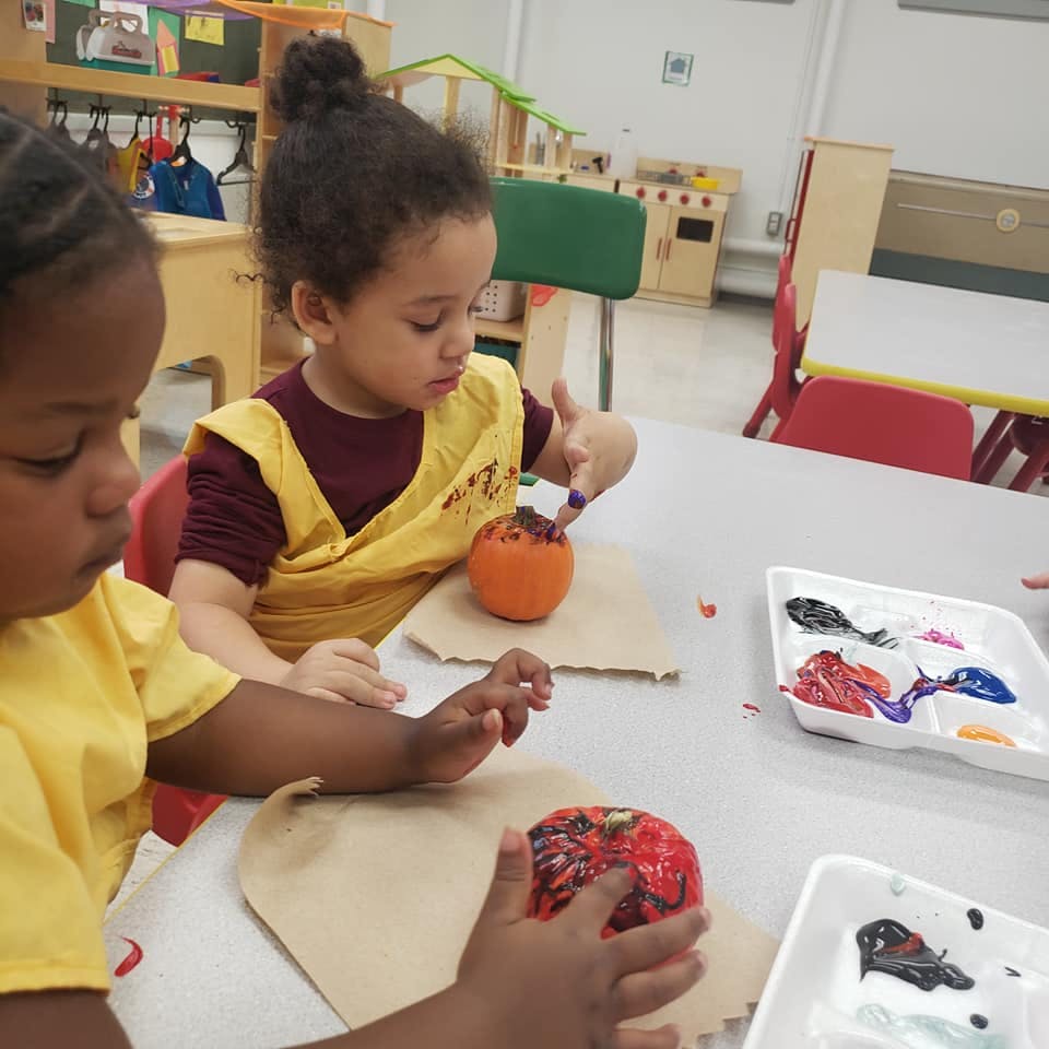 Two children painting small pumpkins at a table