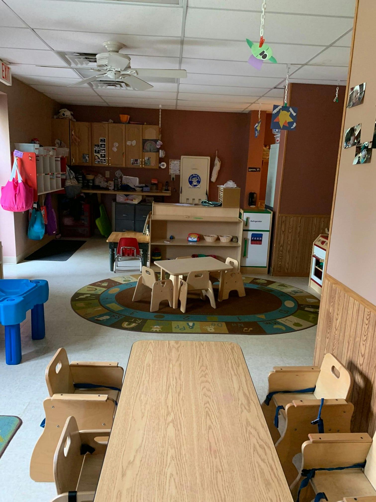 Classroom with small tables and chairs, a rug, and storage cabinets