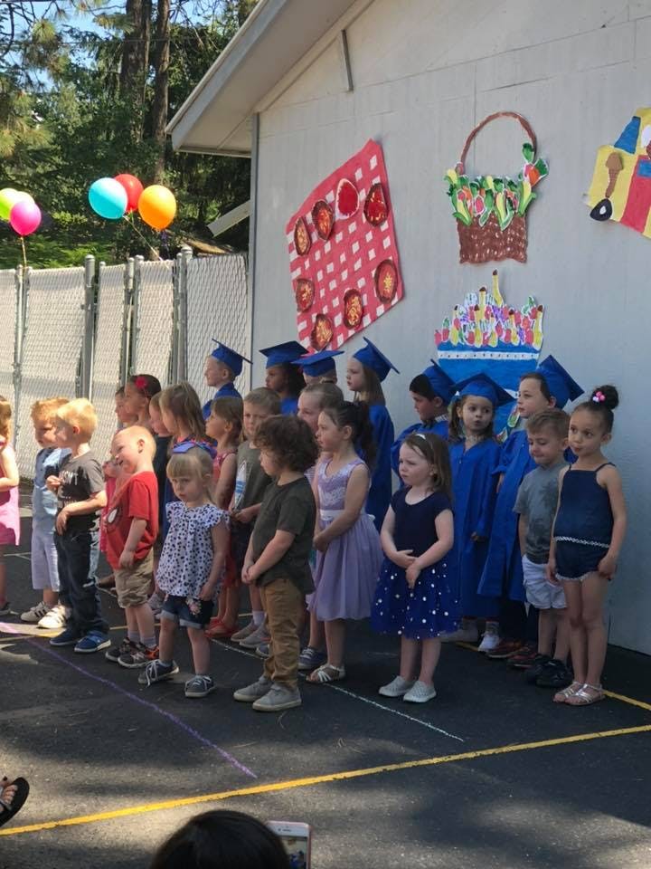 Children and teens in graduation caps and gowns standing in a line outdoors