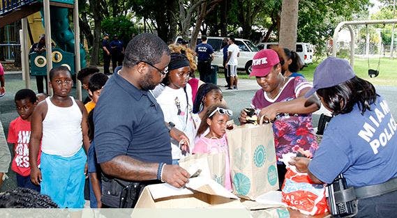 People and children receiving items from a person in a Miami Police shirt