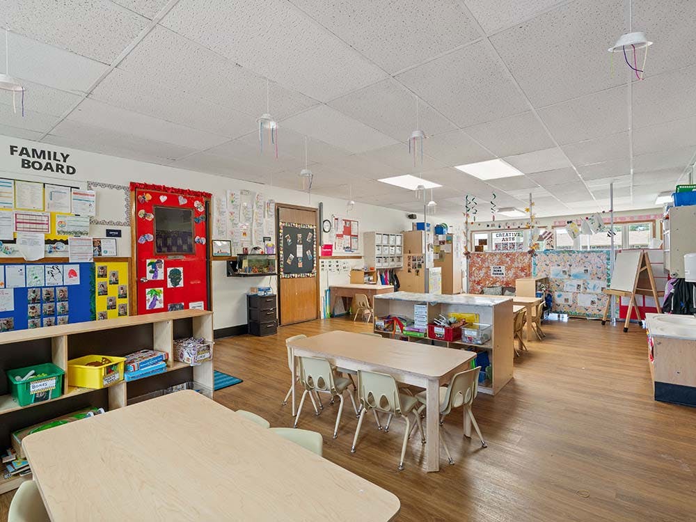 Classroom with child-sized tables and chairs, shelves, and a "Family Board"
