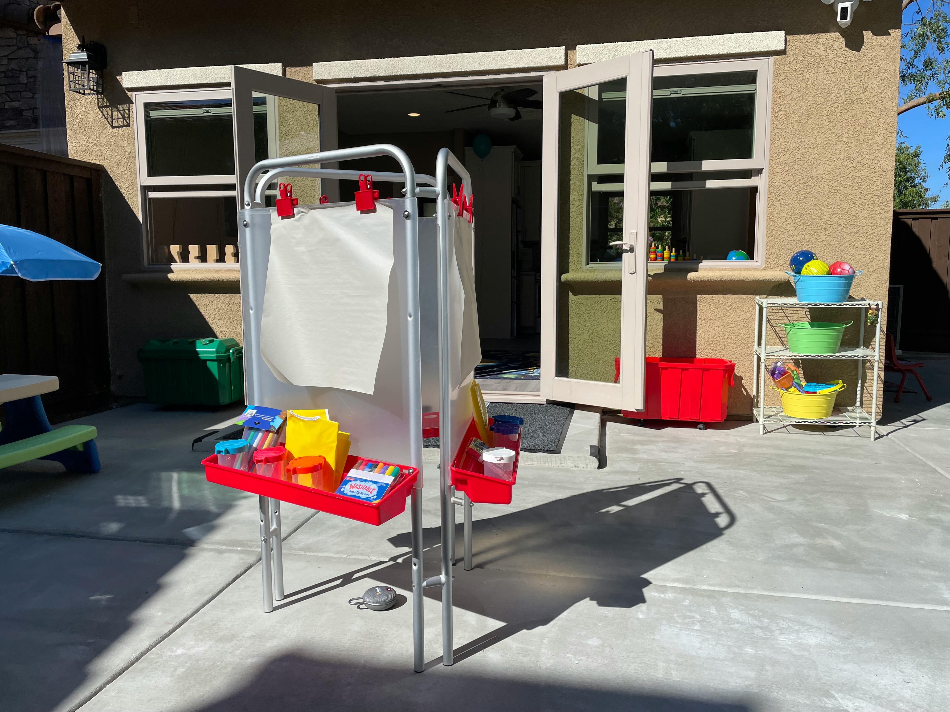 Child's art easel with paper and art supplies on a patio