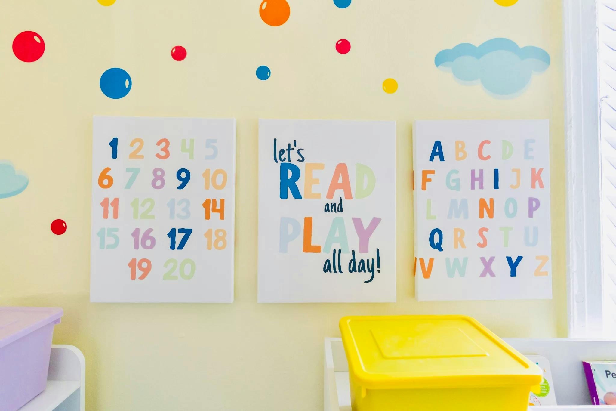 Three educational signs on a wall: numbers 1-20, 'let's READ and PLAY all day!', and the alphabet