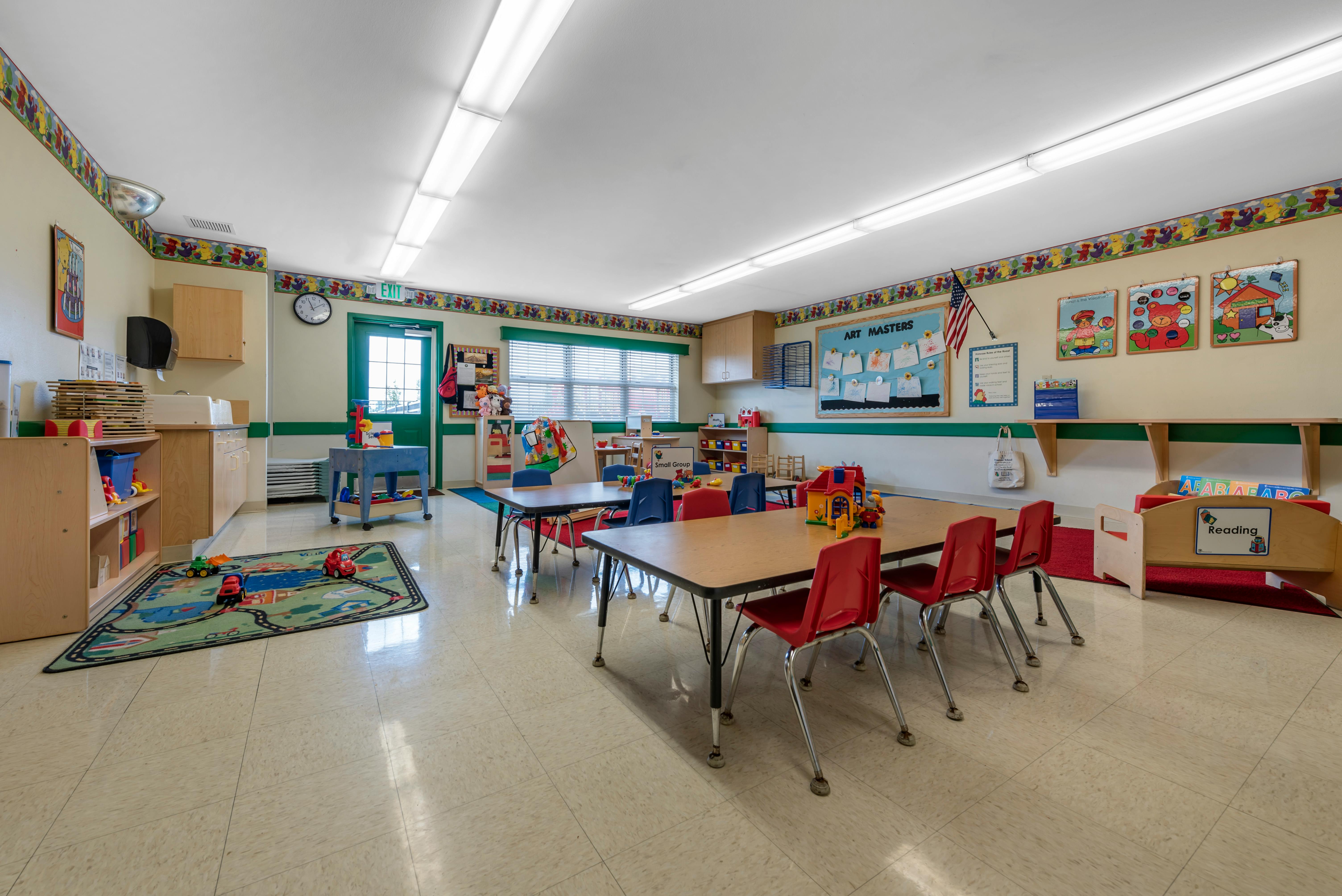 Children's classroom with tables, chairs, play area, and various learning decorations