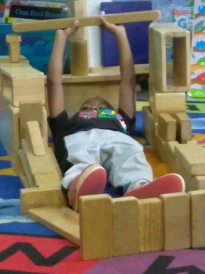 Child lying on back, holding a wooden block above head