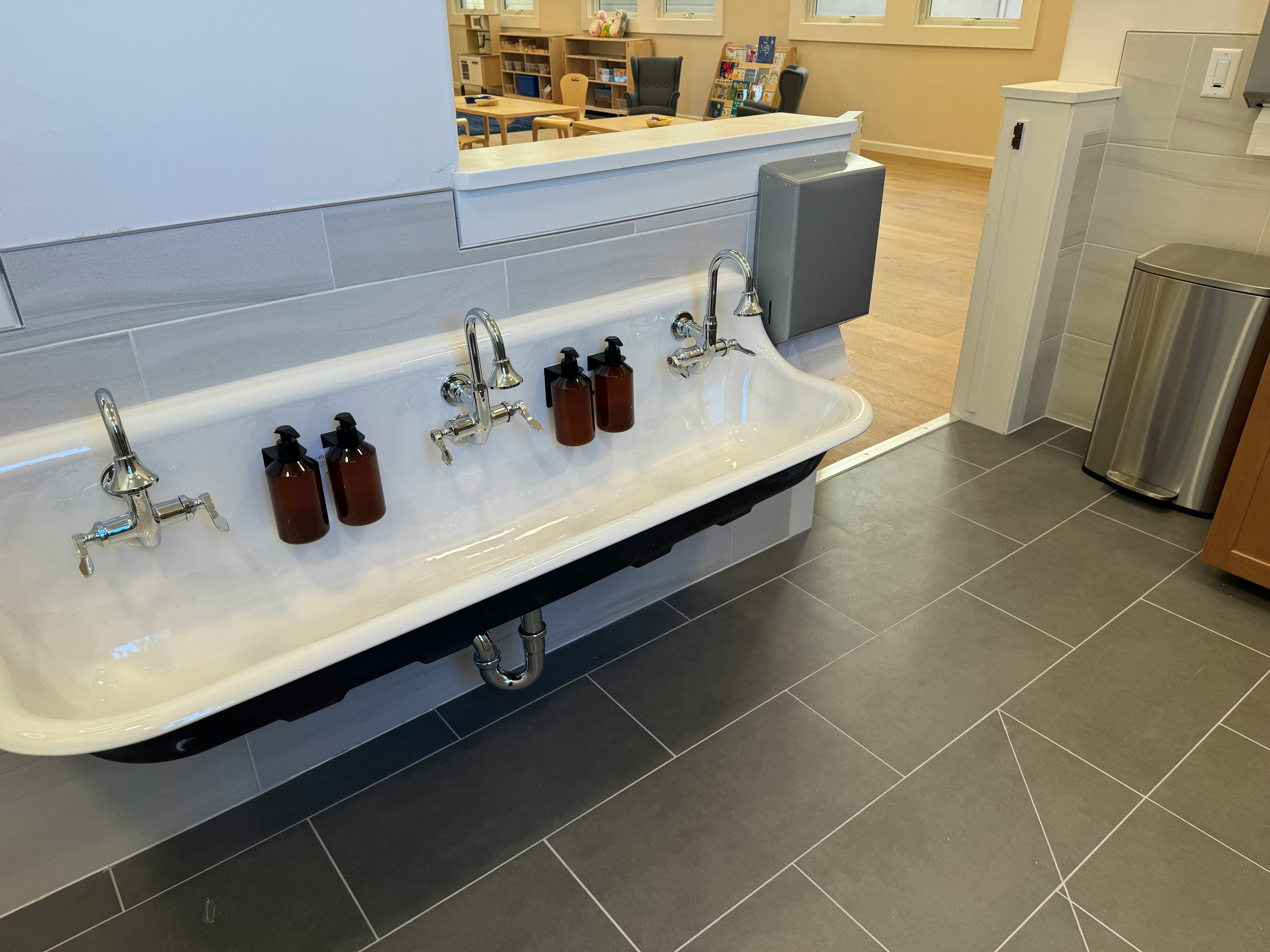 White trough sink with multiple faucets and brown bottles