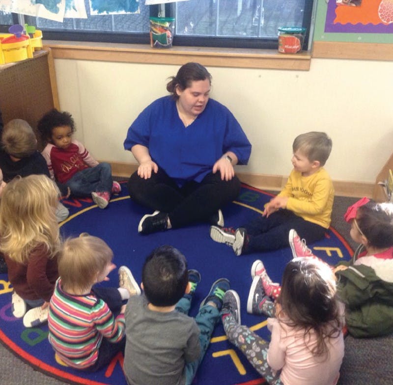 Person sitting on floor with children in a circle of children in a classroom