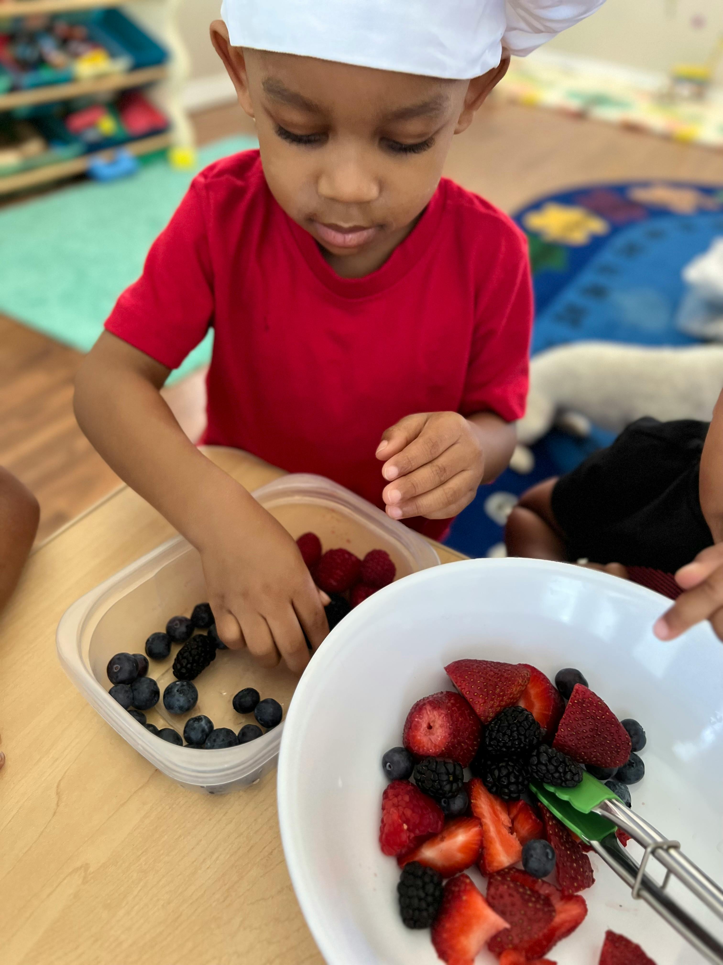 Child in a chef hat picking berries from a container