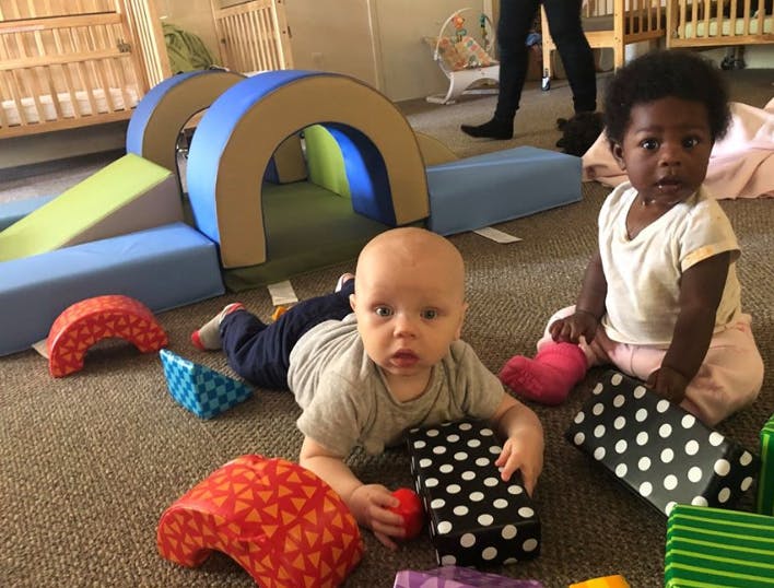Two babies on a carpeted floor with soft play equipment