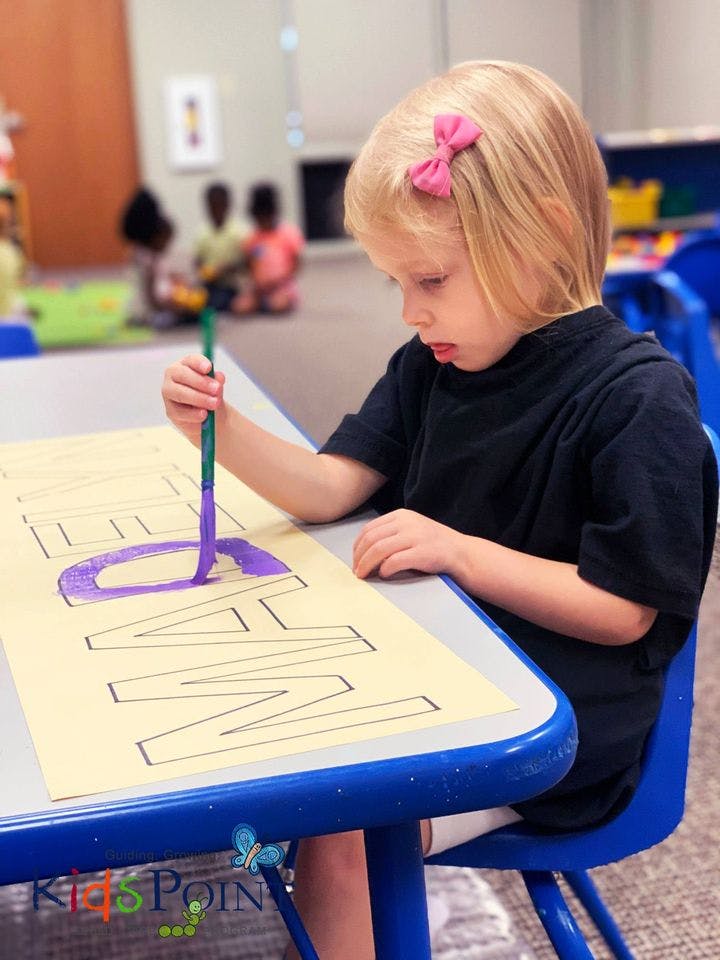 Child painting letters on paper at a table in a classroom