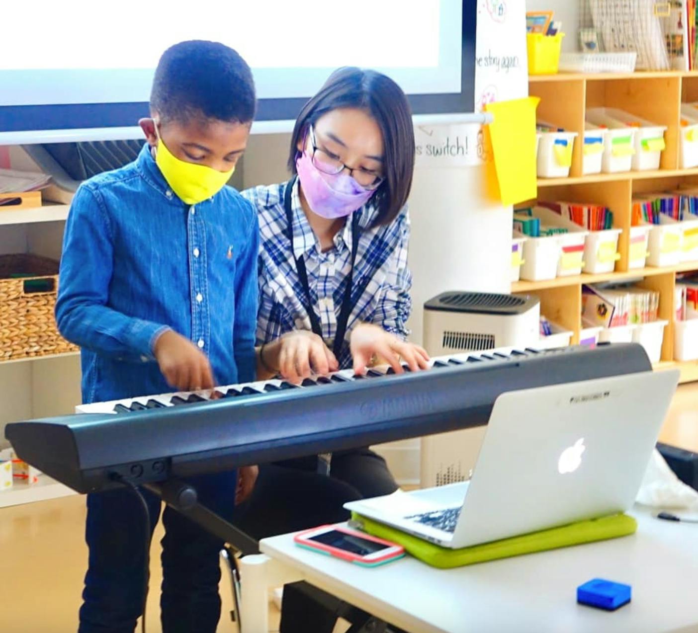 Adult and child wearing masks playing a keyboard