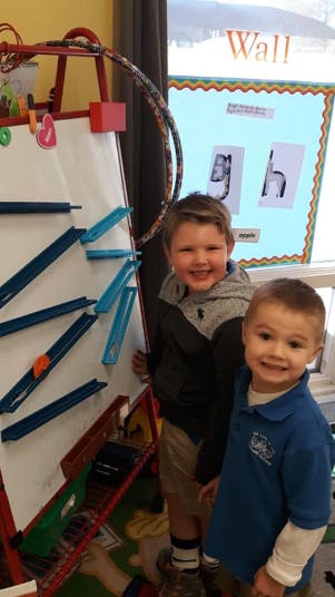 Two children standing next to a white board with blue tracks