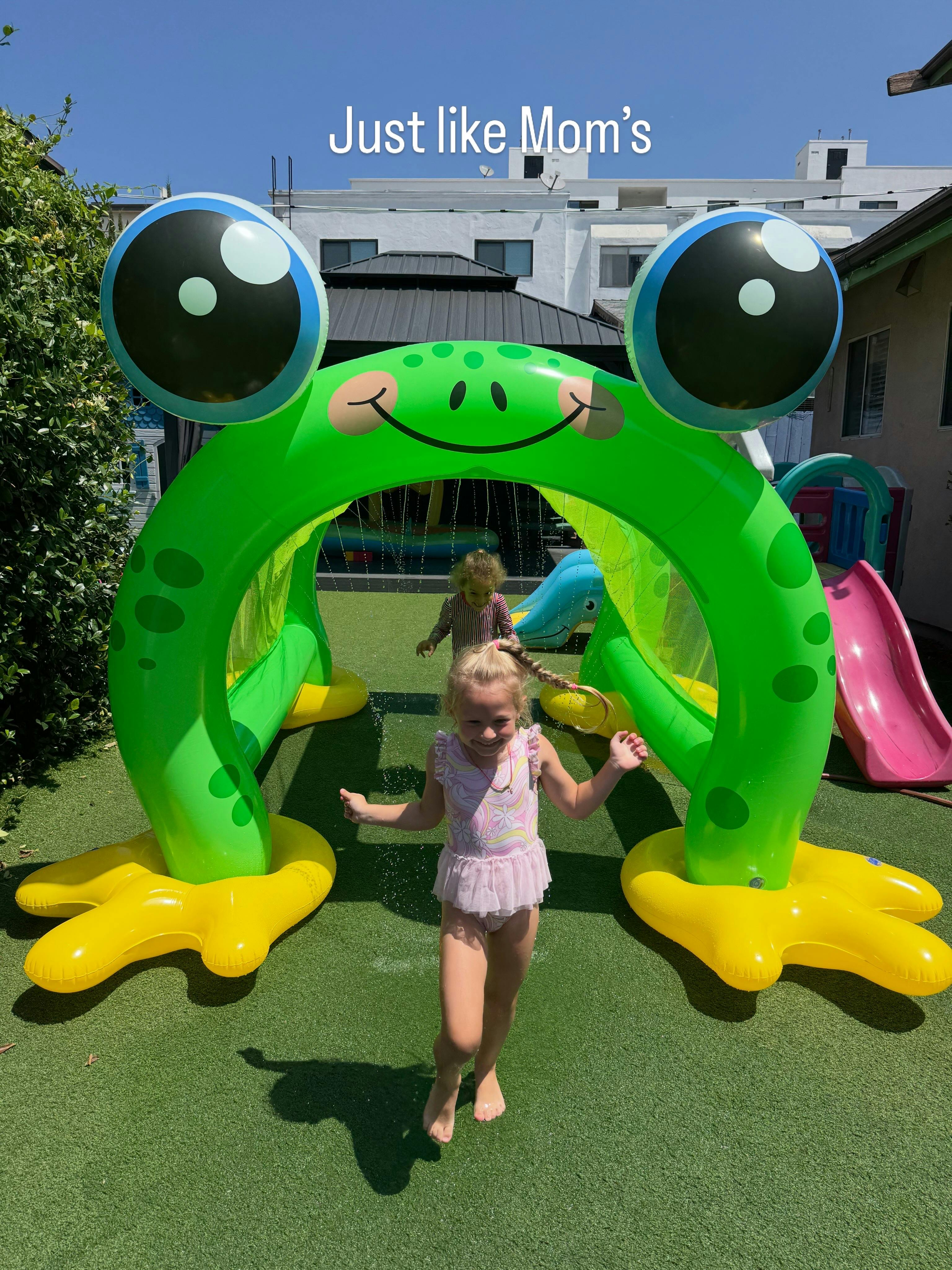 Children playing under an inflatable frog sprinkler in a yard