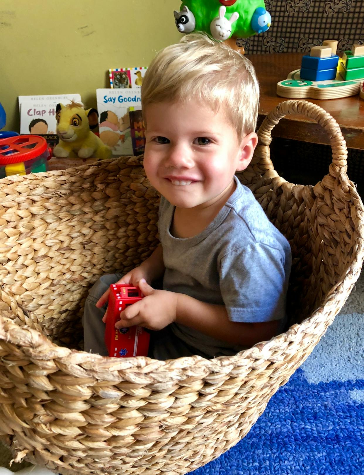 Child sitting in a woven basket holding a red toy