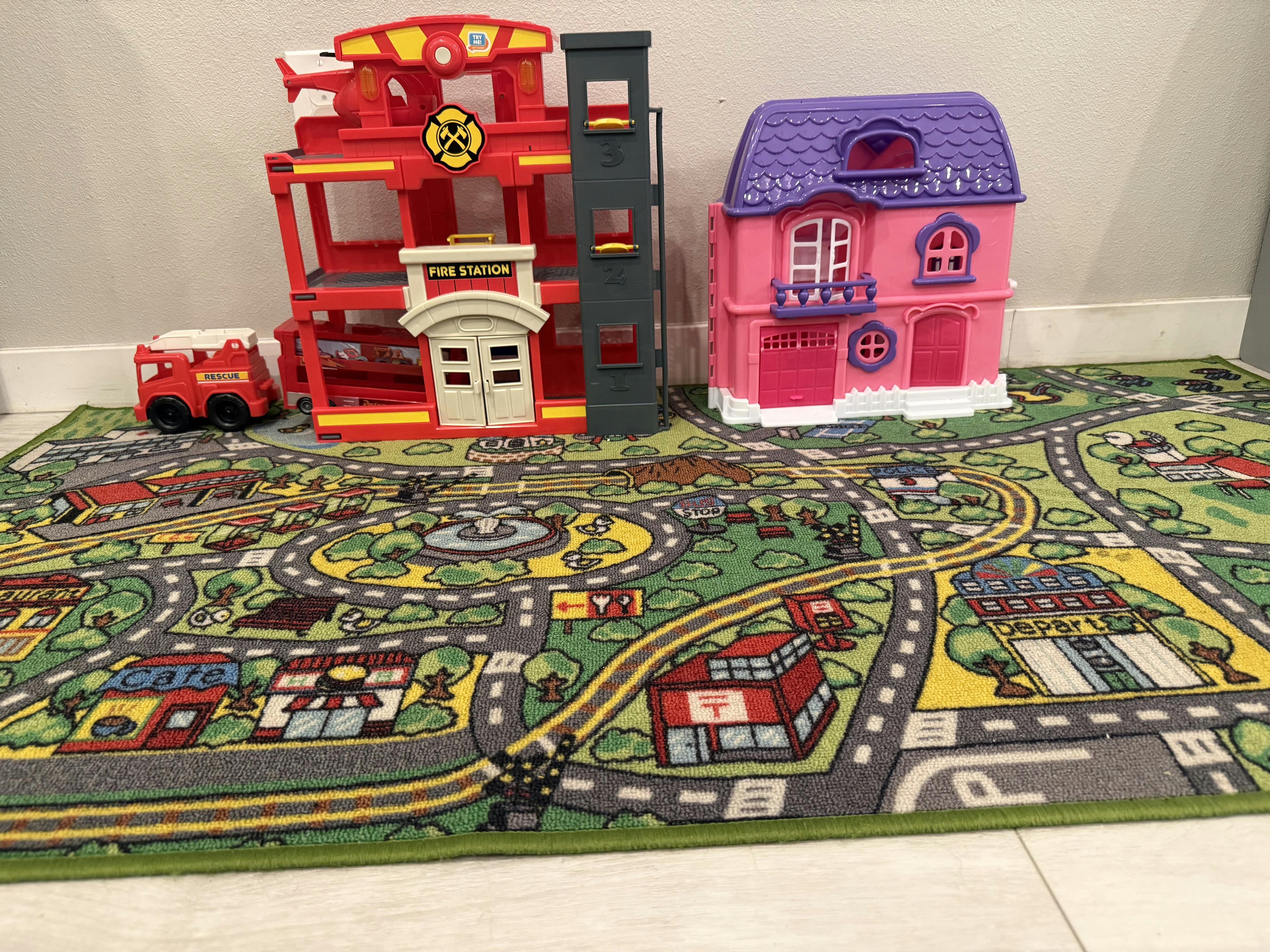 Toy fire station and dollhouse on a play rug with a road pattern