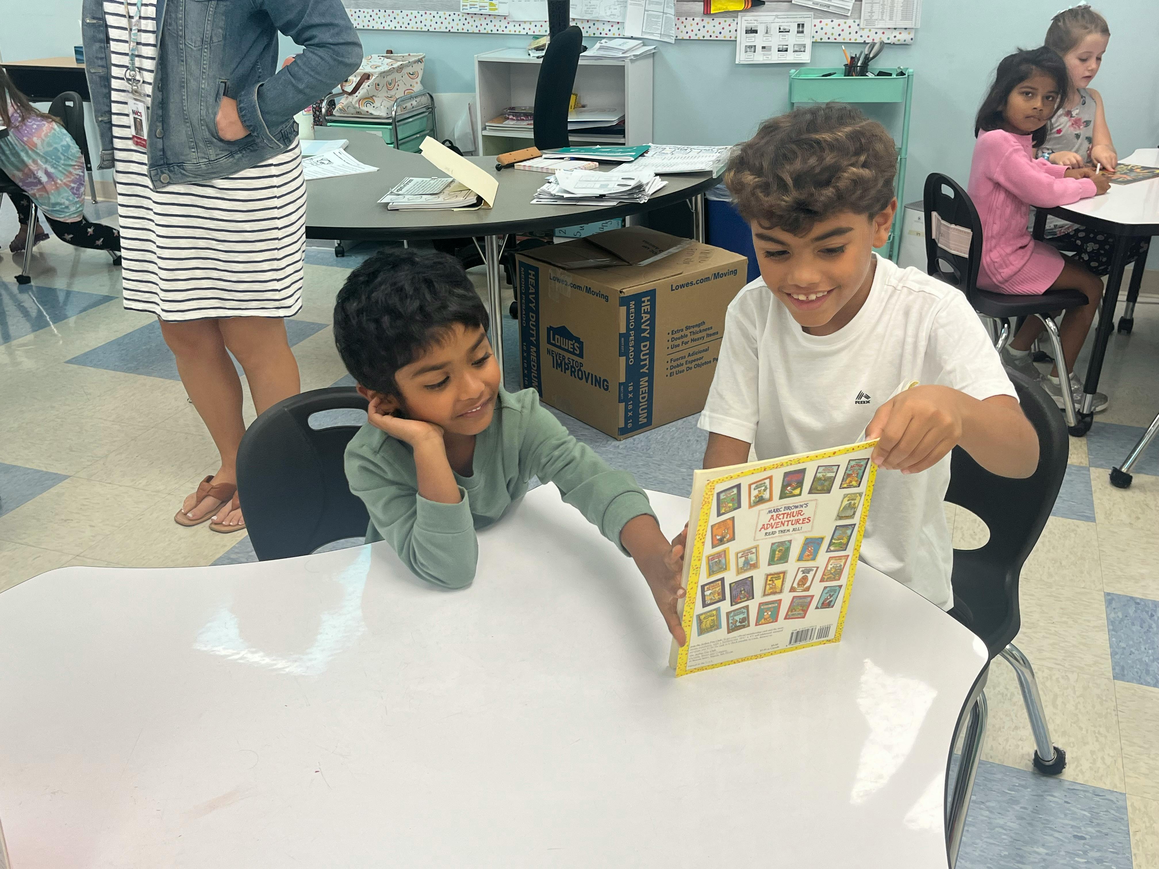 Two children looking at a book in a classroom