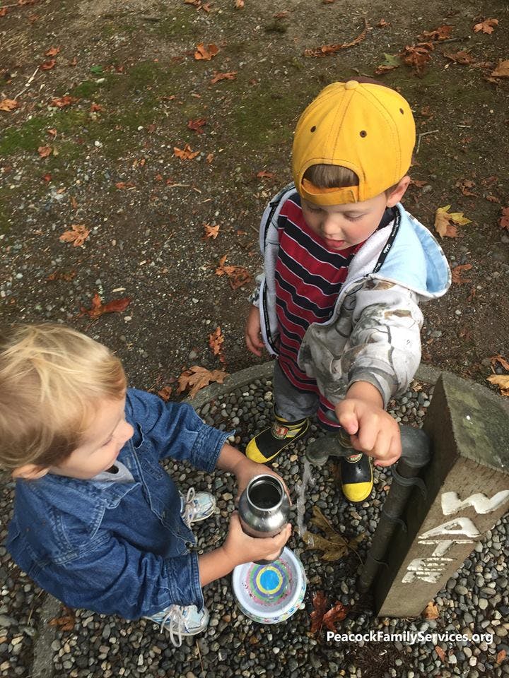 Two children filling a water bottle from an outdoor spigot