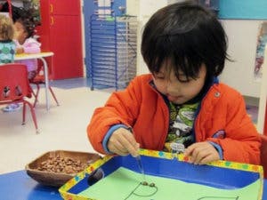 Child playing with beads and string in a classroom