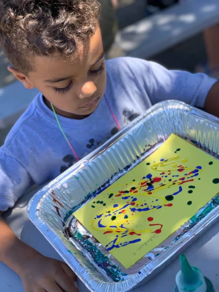 Child looking at a yellow paper with paint splatters in a foil tray