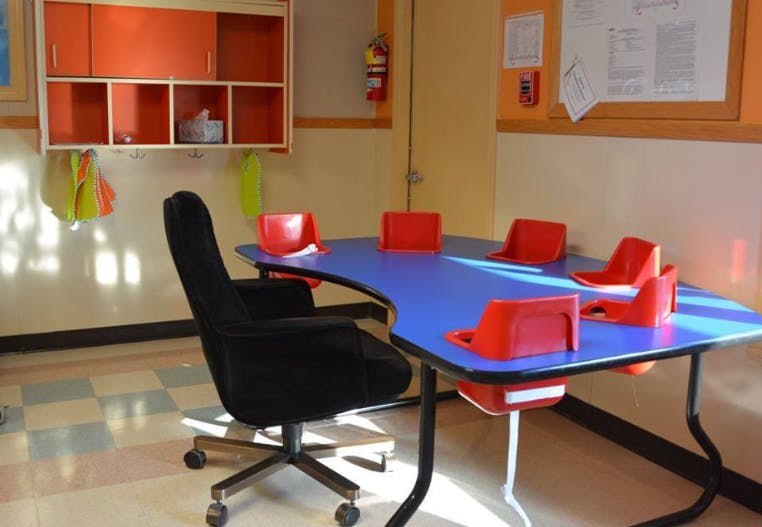 Classroom with blue table, red chairs, and orange cabinets