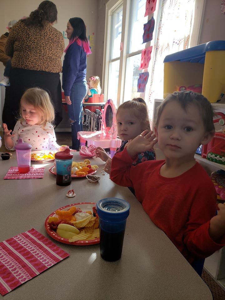 Three children sitting at a table with plates of food and drinks
