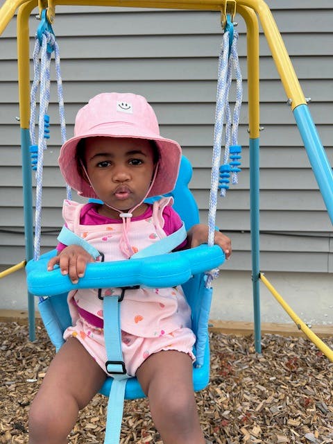 Child in a pink hat sitting in a blue swing