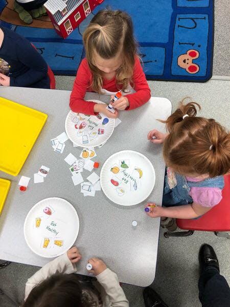 Children gluing cutouts onto paper plates at a table