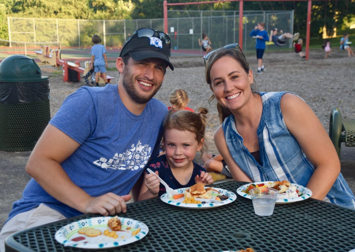 Two adults and a child eating at a picnic table